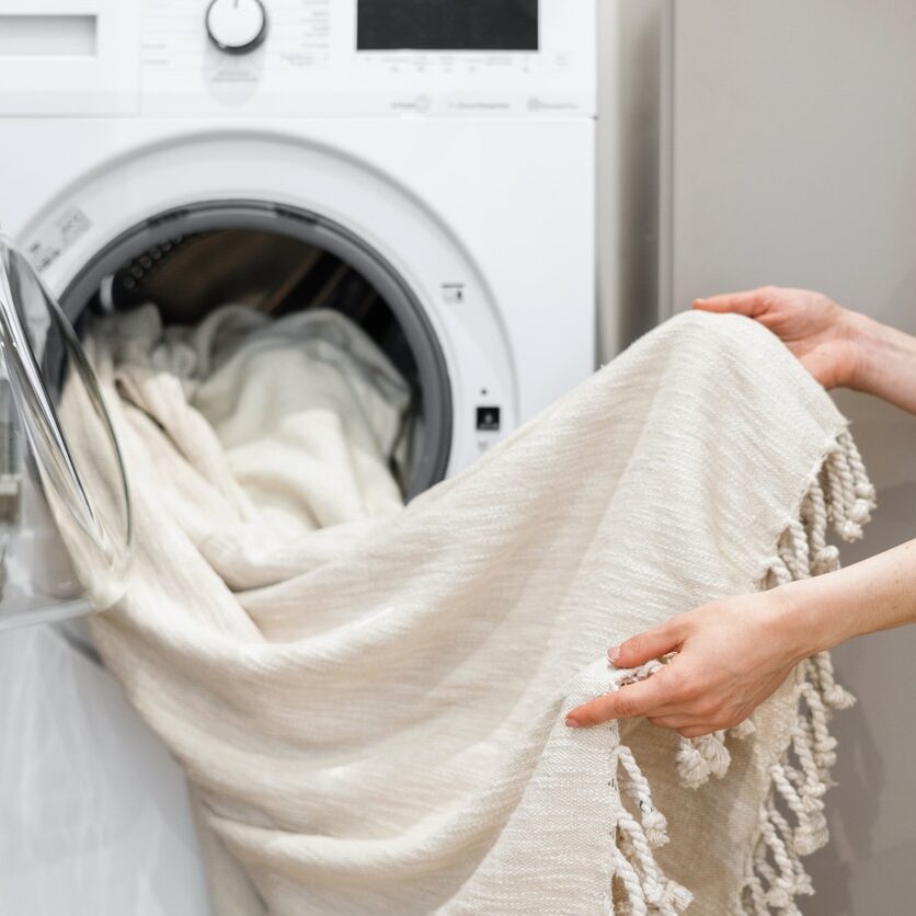 Cropped view of woman unloading laundry from white washing machine. Tulle cleansing. Cleaning service worker. Concept of purity. Housekeeping idea